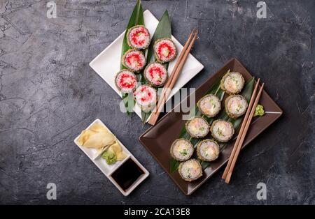 Adagiatevi i panini caldi con avacado, salmone, formaggio cremoso, alghe, salsa di soia, zenzero su un tavolo scuro. Sushi Foto Stock