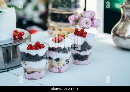 Diversi tipi di deliziosi dolci e dolci ripieni di frutti di bosco e panna bianca in bicchieri sul tavolo Foto Stock