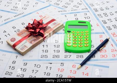 Sullo sfondo del calendario si trova un pacchetto di soldi con un arco rosso, una calcolatrice e una penna Foto Stock