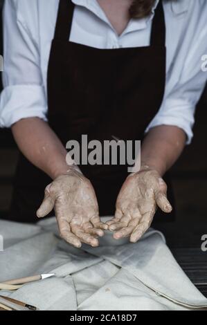 Mani bagnate ricoperte di argilla grigia di vasaio Foto Stock