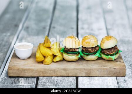 Tre mini hamburger con polpettine di manzo, patatine fritte e maionese su tavola di legno. Sfondo di tabella shabby invecchiato. Cibo insolito servire. Fast food e uno stile di vita malsano. Foto Stock