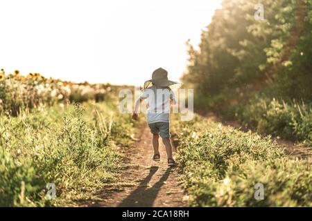 Un ragazzino corre lungo la strada al tramonto godendo della vita e della natura. Felice capretto in campagna. Silhouette di un ragazzo nei raggi solari. Aria fresca, concetto di ambiente. Foto Stock