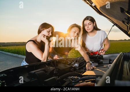 Tre amiche hanno avuto problemi durante il viaggio fuori città, aprire il cofano per controllare i dettagli e cercare di calmarsi Foto Stock