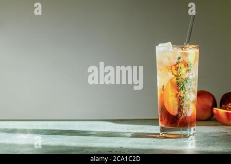 Rinfrescante tè freddo di pesca Cuba Libre o cocktail di tè freddo di Long Island in vetro con paglia. Bevanda estiva alla frutta rinfrescante. Messa a fuoco selettiva Foto Stock