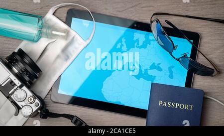 Viaggio sicuro durante una crisi pandemica, scrivania con maschera chirurgica, mappa digitale, passaporto e altri accessori. Foto Stock