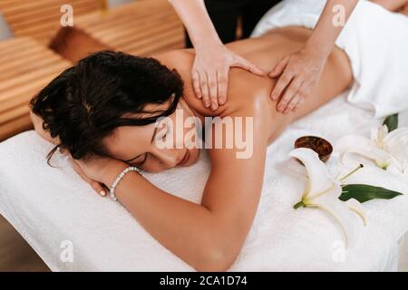 Bella giovane donna nel salone massaggi con capelli ricci marroni e pelle sana. Concetto di massaggiatore e paziente. Foto Stock