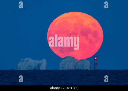 Mudeford, Dorset, Regno Unito. 3 agosto 2020. Regno Unito Meteo. La luna piena di Sturgeon si illumina di rosso mentre si alza da dietro il faro di Needles sull'isola di Wight visto da Mudeford Quay in Dorset in una chiara serata estiva. Picture Credit: Graham Hunt/Alamy Live News Foto Stock