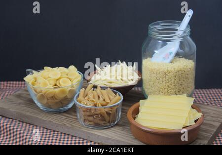 Un tavolo con vari contenitori con alcune paste italiane come i maccheroni integrali, le orecchiette, i trofie, le piastre per i cannelloni e le lettere per s. Foto Stock