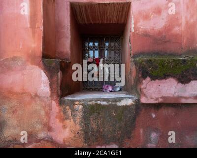 Una finestra con un antico reticolo metallico su una parete rossa nella medina di Marrakech, Marocco Foto Stock