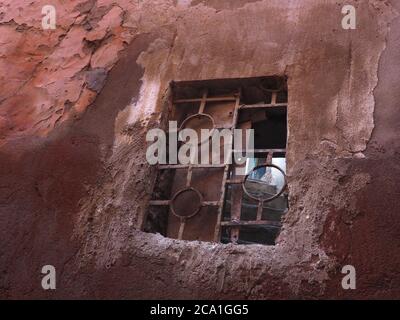 Antica finestra con antica grata di metallo su un muro rosso nella medina di Marrakech, Marocco Foto Stock