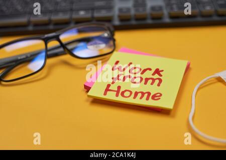 Tastiera per computer, occhiali, maschera facciale e note appiccicose su sfondo giallo con lavoro da home text Foto Stock