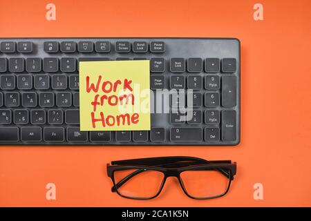 Tastiera per computer, occhiali e note appiccicose su sfondo rosso con lavoro da home text Foto Stock