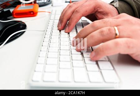 mani maschili tasti di digitazione su una tastiera bianca di un computer in ufficio. Tecnologia e lavoro. Foto Stock