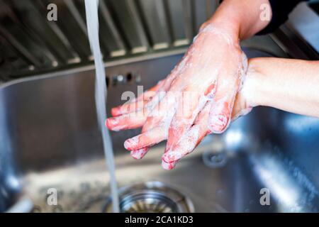 una giovane donna caucasica che le lava le mani con sapone. Coronavirus pandemia COVID-19. Mantenere pulite le mani è uno dei passaggi più importanti per evitare ge Foto Stock