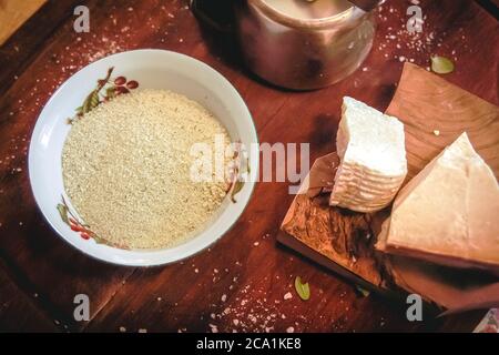 Una ciotola con pinoli tritati e un po' di pecorino e parmigiano su una tavola di legno. Preparazione del pesto. Cucina italiana Foto Stock