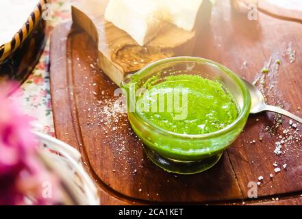 Una ciotola di vetro con salsa di pesto fatta in casa su un tavolo di legno in una cucina rustica italiana. Parmigiano e pecorino. Cucina tradizionale italiana Foto Stock