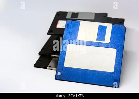 un floppy disk blu con un'etichetta adesiva bianca con un gruppo di altri floppy disk neri impilati sullo sfondo. Tecnologia di storage dei dati obsoleta. Foto Stock