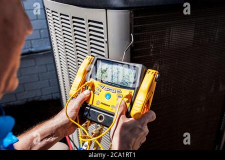 Repairman lavora all'esterno su un condizionatore d'aria di casa utilizzando uno strumento digitale portatile Fieldpiece Foto Stock