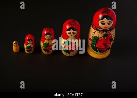 Fila isolata di bambole russe Matrushka fatte a mano su sfondo scuro. Queste statuine femminili tradizionali sono famose nei paesi slavi e queste a Foto Stock