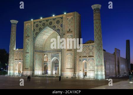 Ulugh Beg Madrasah illuminato di notte in Registan, Samarcanda, Uzbekistan. Edificio islamico con torri e grande iwan decorato con piastrelle in ceramica Foto Stock