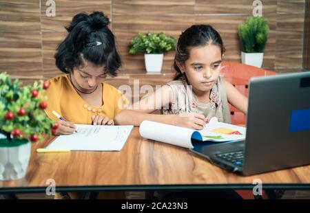 Due bambini impegnati nella scrittura guardando nel portatile durante la lezione online o virtuale a casa - concetto di e-learning o di apprendimento a distanza o bambini Foto Stock