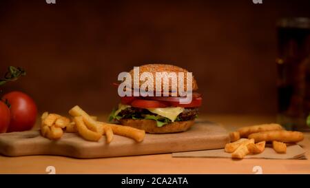 Primo piano con vista su un gustoso hamburger di pancetta appena fatto in casa con patatine fritte su vassoio di legno Foto Stock