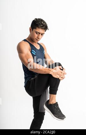 muscolo uomo che indossa i supporti di sportswear di fronte faccia faccia allungare la gamba sollevando la gamba in su davanti allo stomaco su uno sfondo isolato Foto Stock