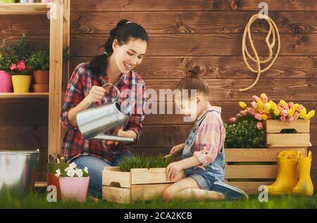 Carino ragazza bambino aiuta la madre a prendersi cura delle piante. Madre e sua figlia si sono impegnate nel giardinaggio nel cortile. Concetto di primavera, natura e cura. Foto Stock