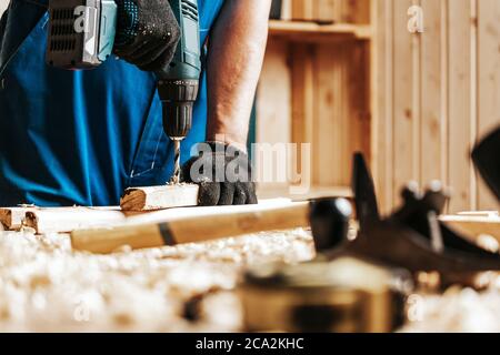 Primo piano di un operaio di costruzione maschio in una costruzione sporca nera nel complesso chiude una vite con un cacciavite moderno nero in un blocco di legno nel w Foto Stock