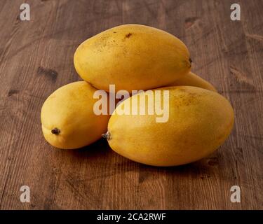 Quattro manga di frutta intera su tavola di legno. Grandi e succulenti frutti gialli maturi su sfondo scuro Foto Stock