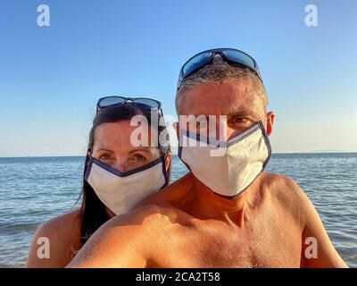 Uomo e donna che prendono selfie sulla spiaggia indossando maschere in tempo invidiabile Foto Stock