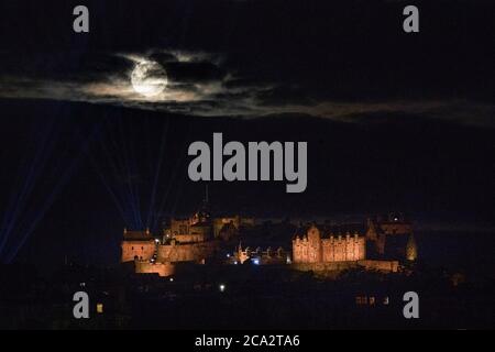 La luna piena, conosciuta come Sturgeon Moon nel mese di agosto, sorge attraverso le nuvole sopra il Castello di Edimburgo. Foto Stock