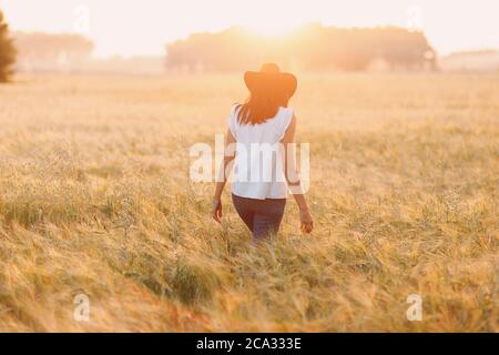Donna contadina in cappello cowboy a campo agricolo al tramonto. Vista posteriore. Foto Stock