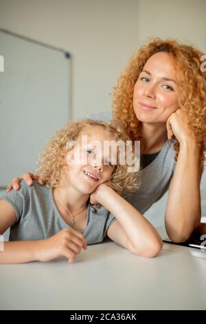 Niente potrebbe separarli o rompere questo amore. Ritratto emotivo di madre frizzy con capelli pelosi che abbracciava la sua adorabile figlia bionda riccia, sorridendo alla macchina fotografica Foto Stock