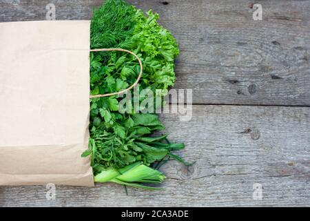 Verdure fresche in un sacchetto di carta - cipolle verdi, aneto, prezzemolo, spinaci, rucola, sorbetto. Consegna a domicilio di alimenti e verdure fresche. Sfondo di legno Foto Stock