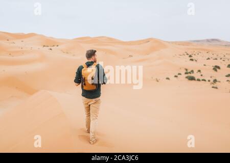 Uomo zaino in spalla viaggio in Marocco, deserto del Sahara. Esplora la natura africana, le dune di sabbia intorno. Vista da dietro. Foto Stock