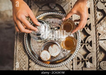 Le mani della donna servono la tradizionale cerimonia marocchina del tè alla menta con biscotti e teiera d'argento vintage. Ospitalità e servizio in Marocco, Marrakech. Foto Stock