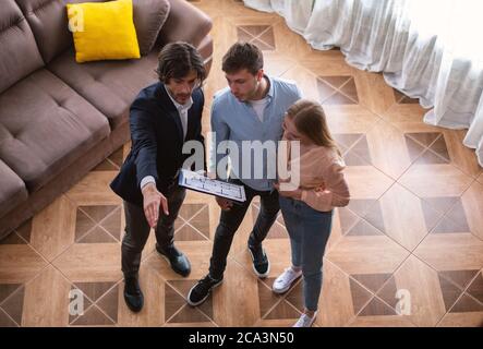 Immobiliare con pianta casa che mostra giovane coppia intorno proprietà in vendita, vista sopra Foto Stock