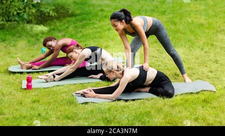 Istruttore di Yoga che aiuta il gruppo di giovani donne a tendere correttamente durante la pratica all'aperto Foto Stock