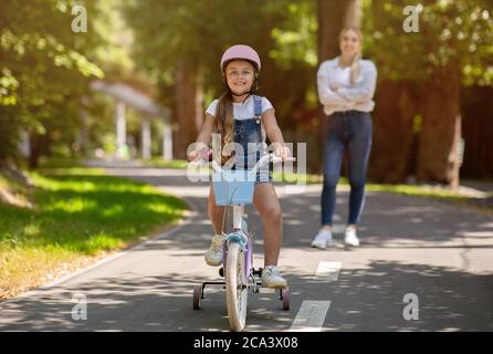 Happy Little Girl Riding bicicletta trascorrere giorno con mamma all'aperto Foto Stock