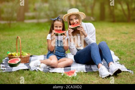 Adorabile madre e figlia che mangiano l'anguria seduta su Plaid Outdoor Foto Stock