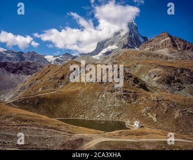 Questa è la famosa montagna del Cervino dal lago alpino di Schwarzsee con la sua piccola cappella che guarda in direzione del prominente crinale di Hoernli al centro, Il percorso seguito da Edward Whymper durante la prima e tragica salita del 15 luglio 1865, quando alcuni dei suoi compagni caddero per tutta la lunghezza della faccia nord. Il crinale all'estrema destra è lo Zmuttgrat. L'iconico Cervino è il cuore e l'anima della città svizzera di villeggiatura montana di Zermatt, nel Cantone svizzero del Vallese, così come lo era nel 2000 Foto Stock