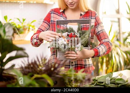 donna fiorista non riconoscibile dal taglio corto con capelli biondi che reggono la composizione meravigliosa delle piante, indossando la camicia casual rossa Foto Stock