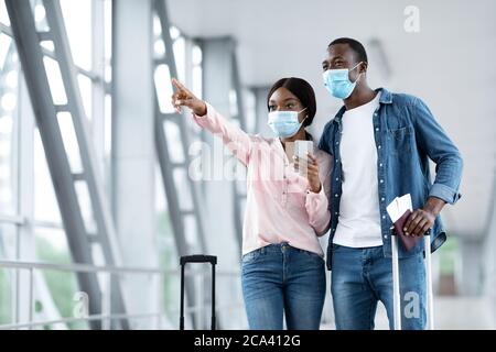 Verso il cancello. Coppia africana in maschere protettive camminando insieme all'aeroporto Foto Stock