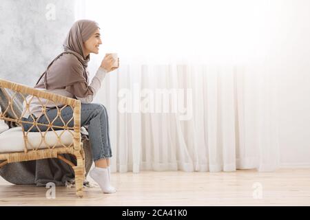 Mattina rilassata. Donna araba riposante in sedia di vimini a casa con il caffè Foto Stock