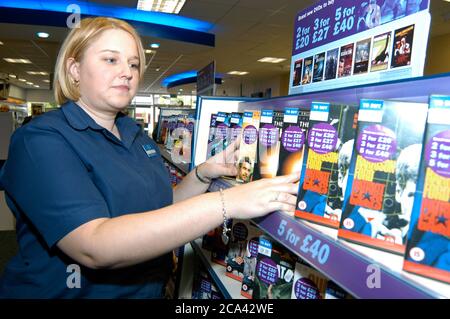 Giovane donna che lavora nel negozio di video noleggio Blockbuster; scaffali impilabili; Merseyside; UK Foto Stock