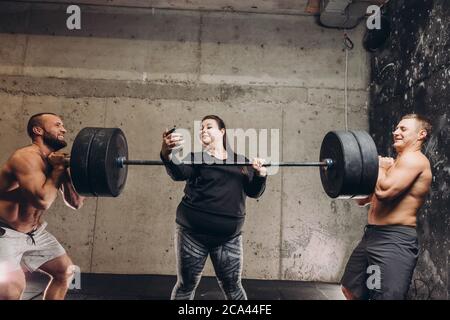 pazzesca ragazza grassa scattando una foto di se stessa mentre gli sportivi sollevano il barbell. primo piano foto. divertimento Foto Stock