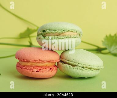 tre macaron rotondi multicolore al forno, il dessert giace l'uno sopra l'altro su uno sfondo verde, primo piano Foto Stock