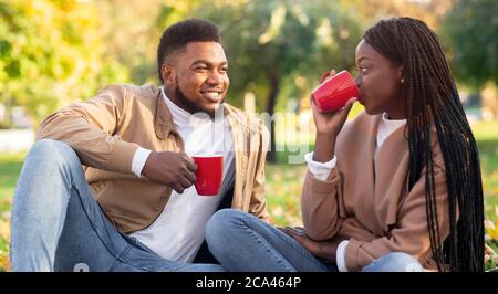 Romantica coppia nera che beve tè all'aperto, gustando un picnic nel parco autunnale Foto Stock