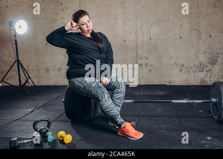 giovane donna groppa seduta sul barbell. esaurimento dopo l'allenamento. foto a lunghezza intera. perdita peso.allenamento difficile Foto Stock